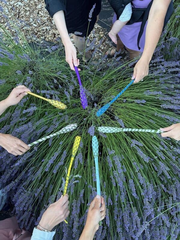 Workshop guests holding their colorful finished lavender wands in a circle over the lavender field